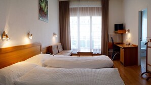A hotel room with two beds, a desk, a chair, a TV, and a window with curtains. - Hotel Victoria (Brig)