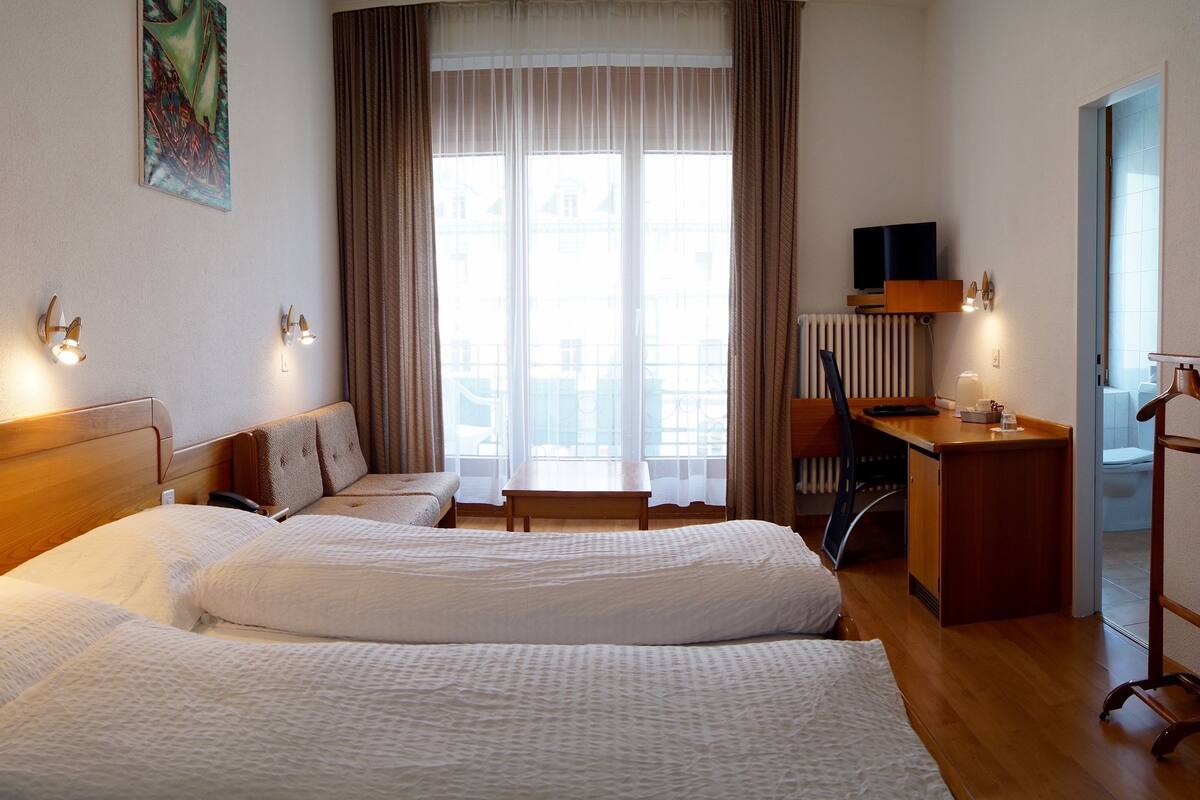 A hotel room with two beds, a desk, a chair, a TV, and a window with curtains.
