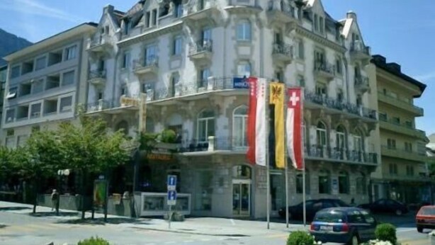 A multi-story hotel with a classic architectural style, featuring balconies and a prominent corner tower. - Hotel Victoria (Brig)