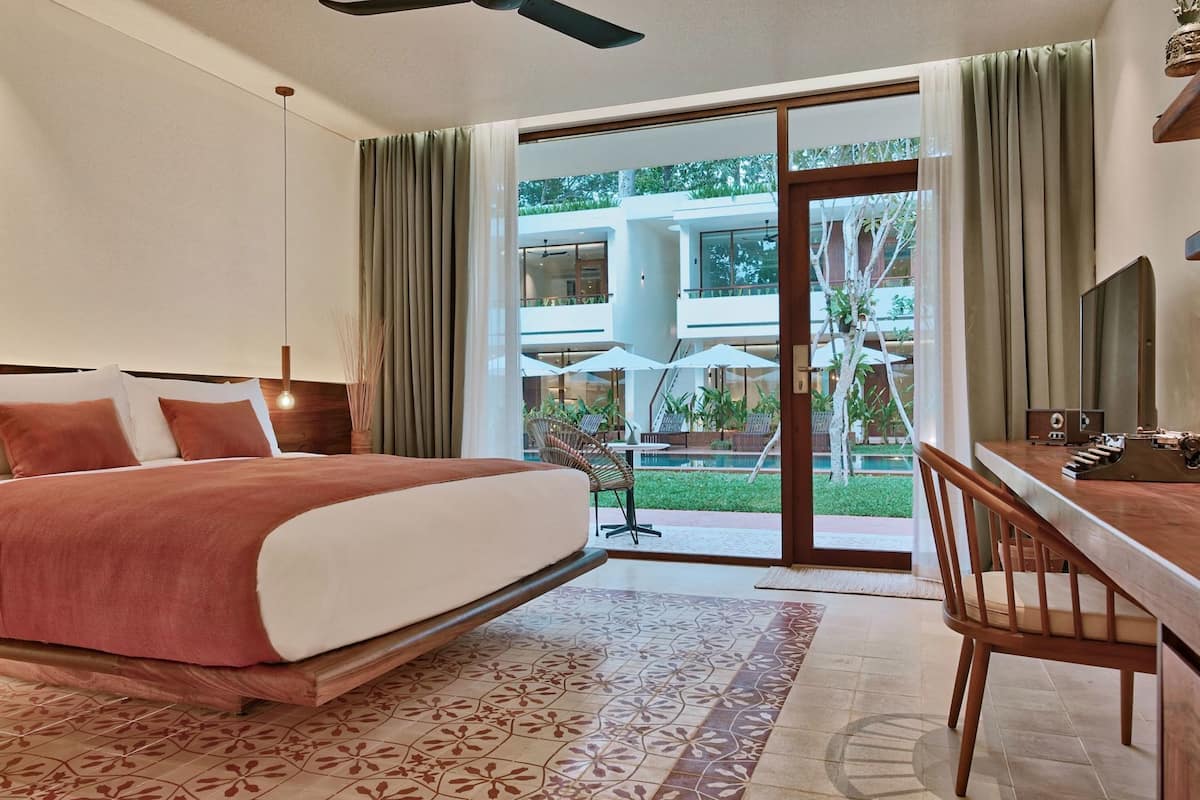A hotel room with a bed, a desk, a chair, a large window, and a view of a pool and outdoor area.