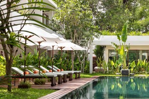 A poolside area with lounge chairs and umbrellas, surrounded by lush greenery and a modern building. - FCC Angkor by Avani (Siem Reap)