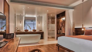Een moderne hotelkamer met een houten vloer, een groot bed, een bureau met een stoel, een kaptafel met een spiegel en een douchegedeelte.