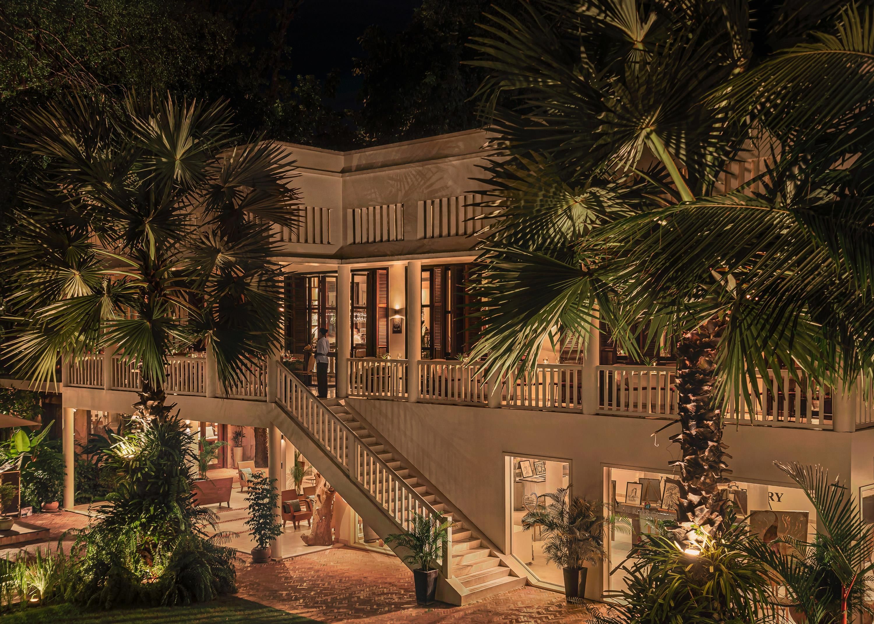A multi-level building with a staircase, palm trees, and a well-lit interior.