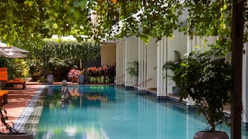 A swimming pool with a tiled edge, surrounded by potted plants and a white wall.
