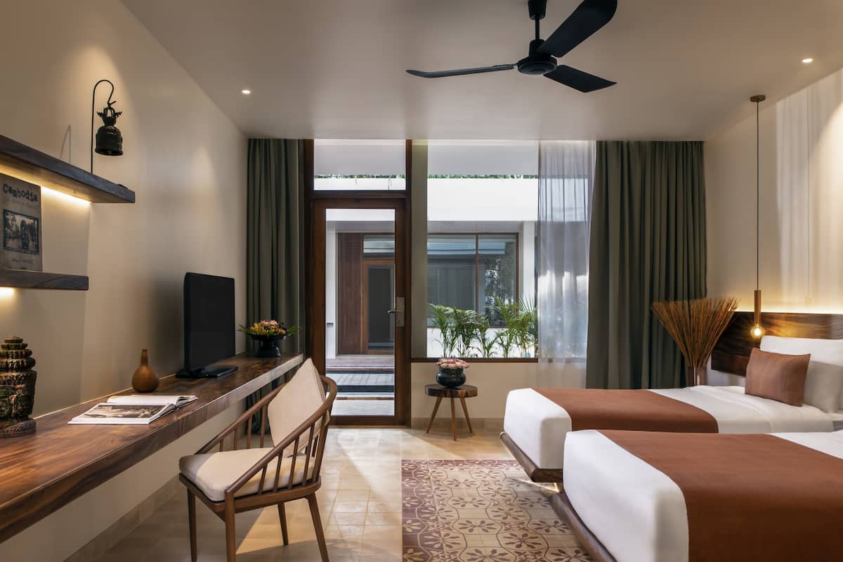 A hotel room with a desk, two beds, a ceiling fan, and a view of the outside.
