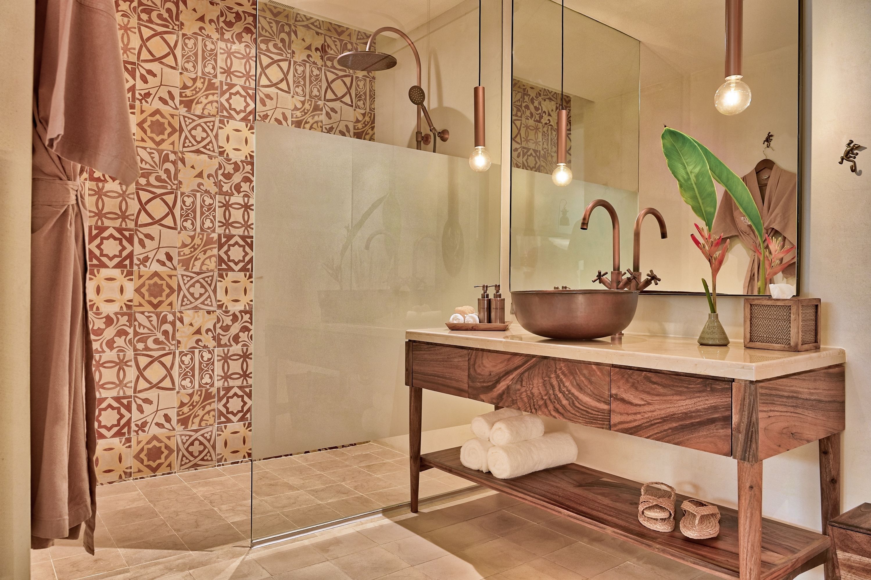 A bathroom with a large mirror, a wooden vanity, a large bowl sink, and a shower with a unique showerhead.