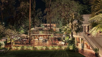 An outdoor dining area with tables and chairs, surrounded by lush greenery and trees.