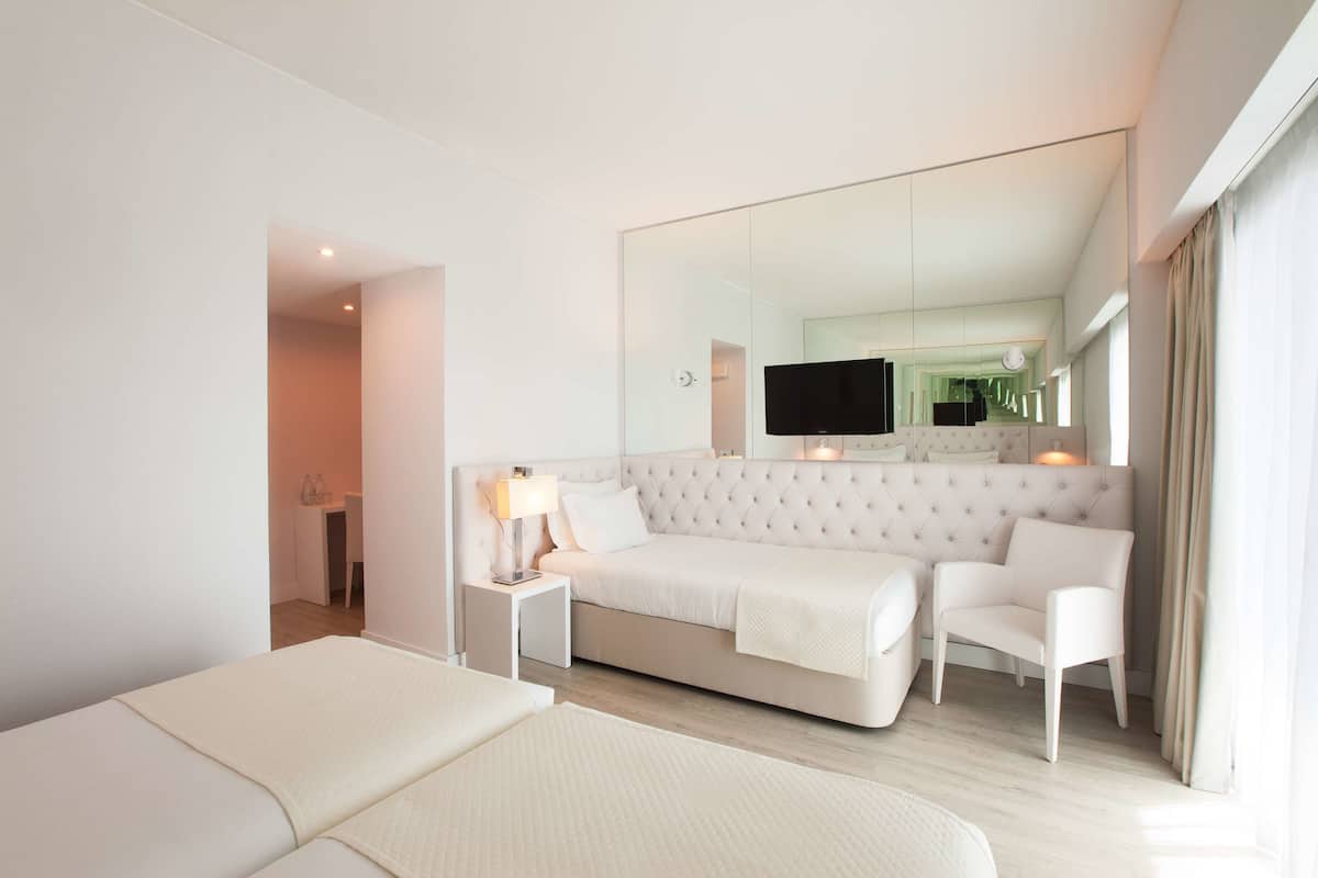 A modern hotel room with a large bed, a sofa, a TV, and a mirror.