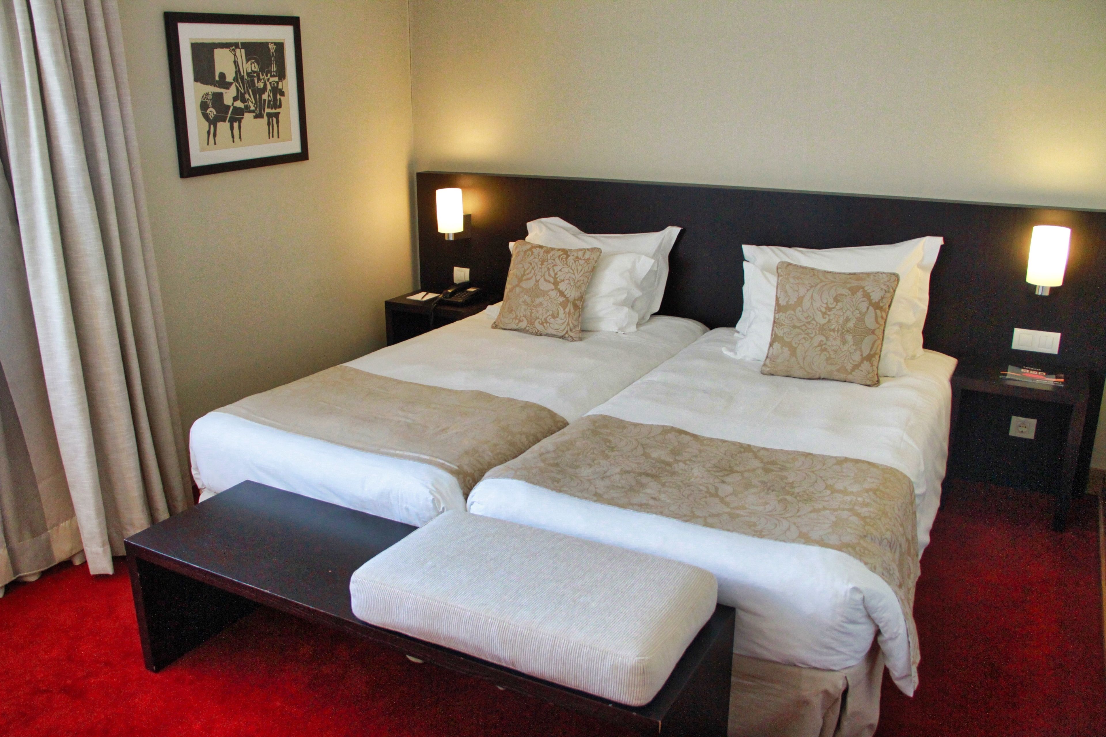 A double bed with two pillows, a bedside table with a lamp, and a bench.