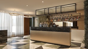 Un moderno vestíbulo de hotel con piso de mármol, una mesa de recepción y una zona de bar con botellas y vasos.