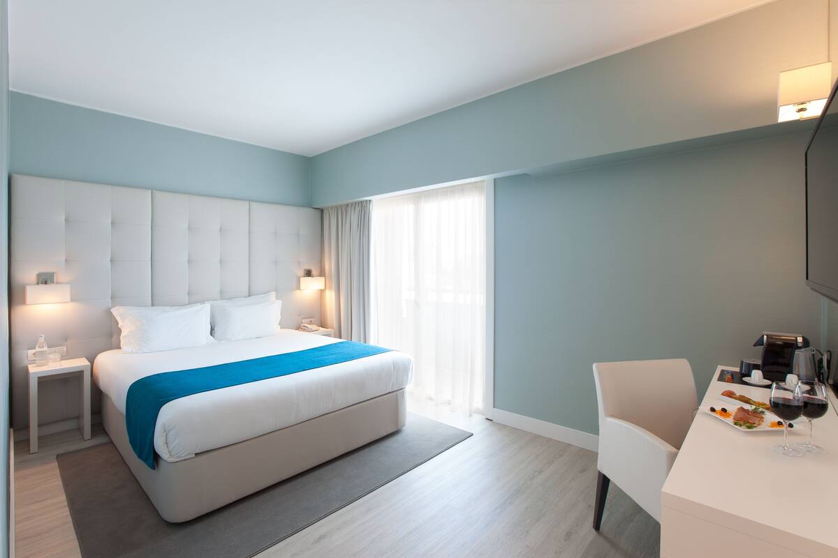 A modern hotel room with a large bed, bedside tables, a desk with a chair, and a TV.