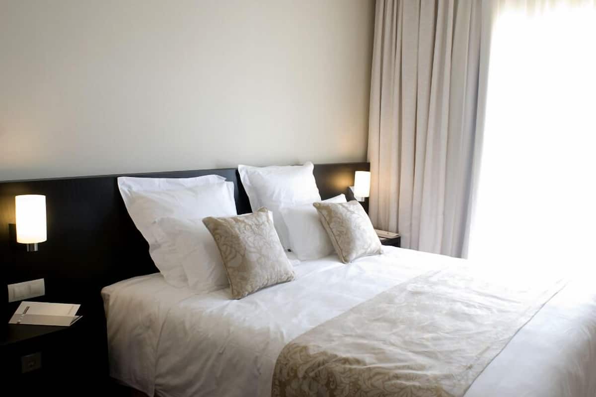 A hotel room with a large bed, two bedside lamps, and a window with curtains.