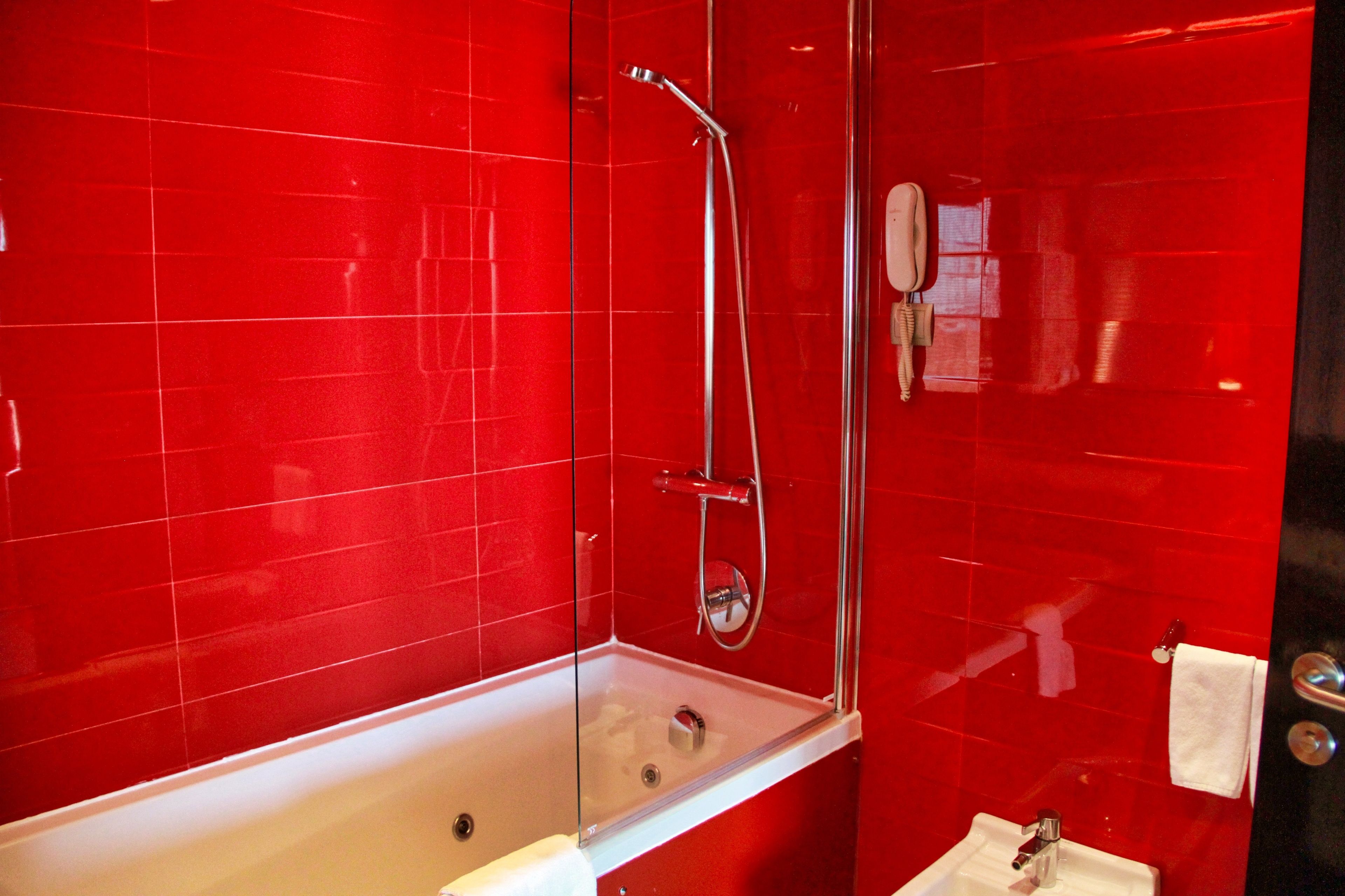 Une salle de bain moderne avec des carreaux rouges, une douche en verre, une baignoire blanche et un lavabo avec un miroir.