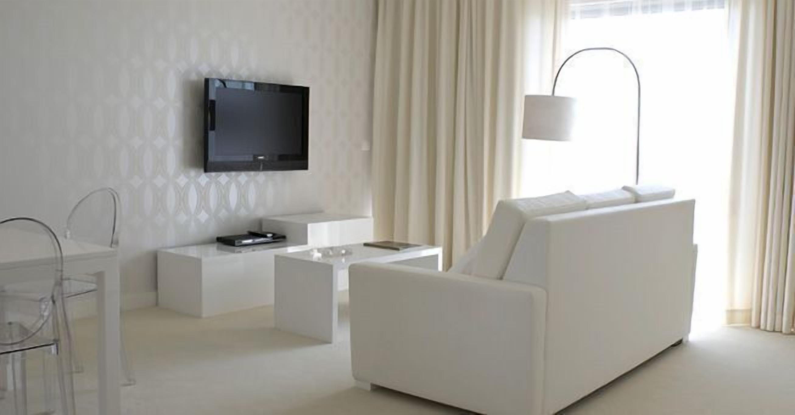 Una sala de estar moderna con un sofá blanco, un televisor de pantalla plana en la pared, una mesa de centro y una lámpara.