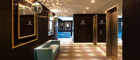 Un hall d’hôtel moderne avec un sol à motifs géométriques, un canapé bleu clair et une boule à facettes.