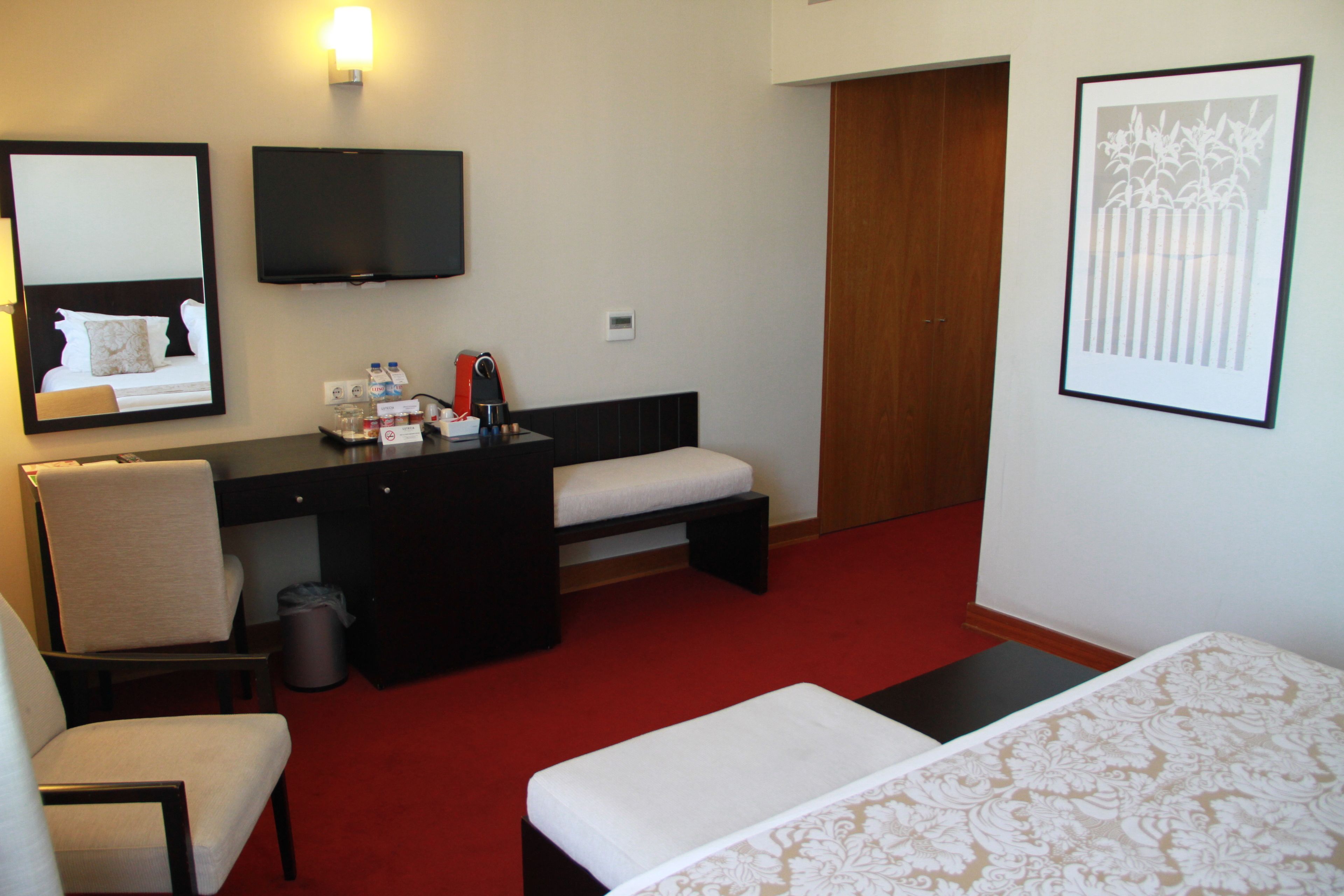 A hotel room with a bed, a desk with a chair, a television, and a framed picture on the wall.