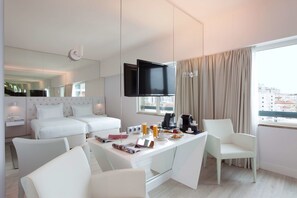 A modern hotel room with a dining area, a bed with white bedding, a flat-screen TV, and a city view. - Lutecia Smart Design Hotel (Lisbon)