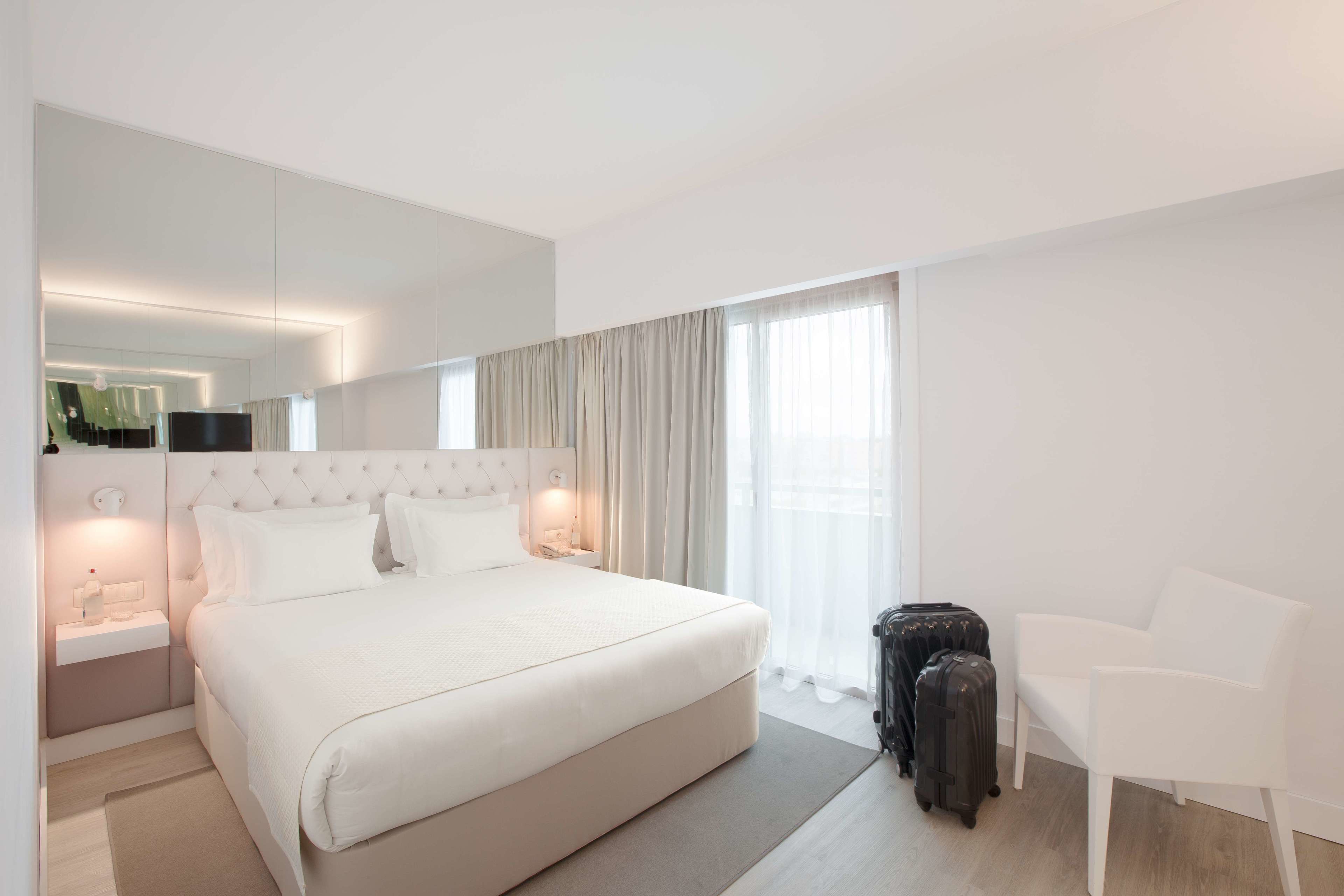 A hotel room with a large bed, bedside tables, a chair, and a suitcase.