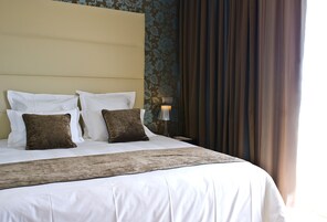 A neatly made bed with white linens and two brown pillows, a headboard, and a wall with floral wallpaper.