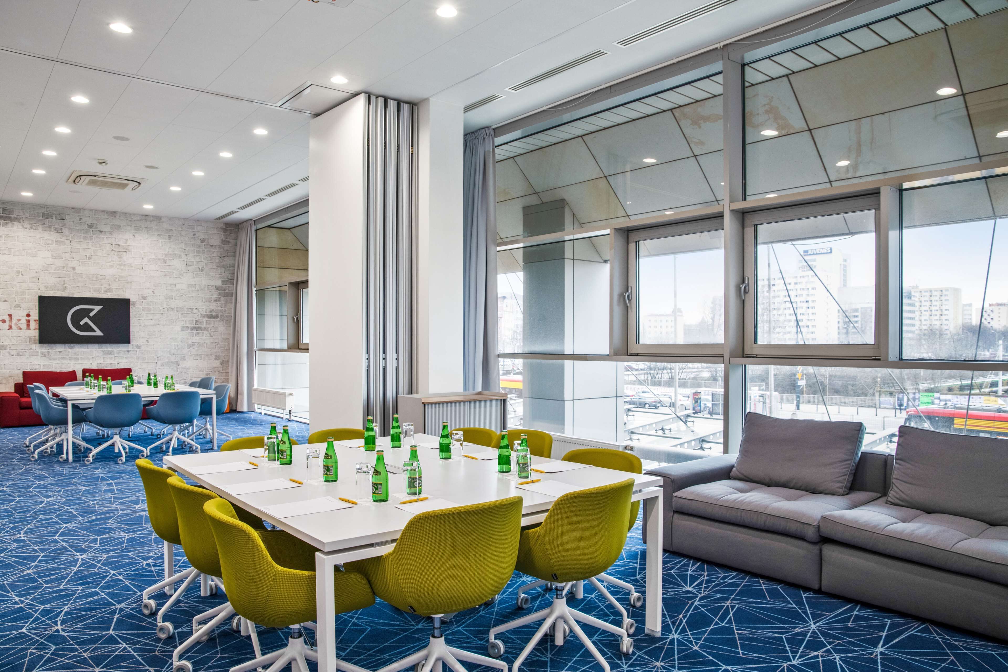 A modern conference room with a large table, yellow chairs, and a grey sofa.