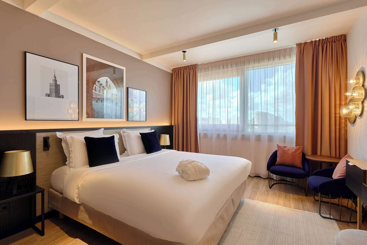 Ein Hotelzimmer mit einem großen Bett, einem Schreibtisch, zwei Stühlen und einem fenster mit Vorhängen.