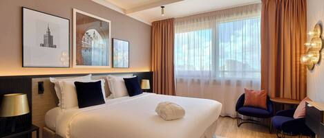Habitación de hotel con una cama grande, un escritorio, dos sillas y una ventana con cortinas.