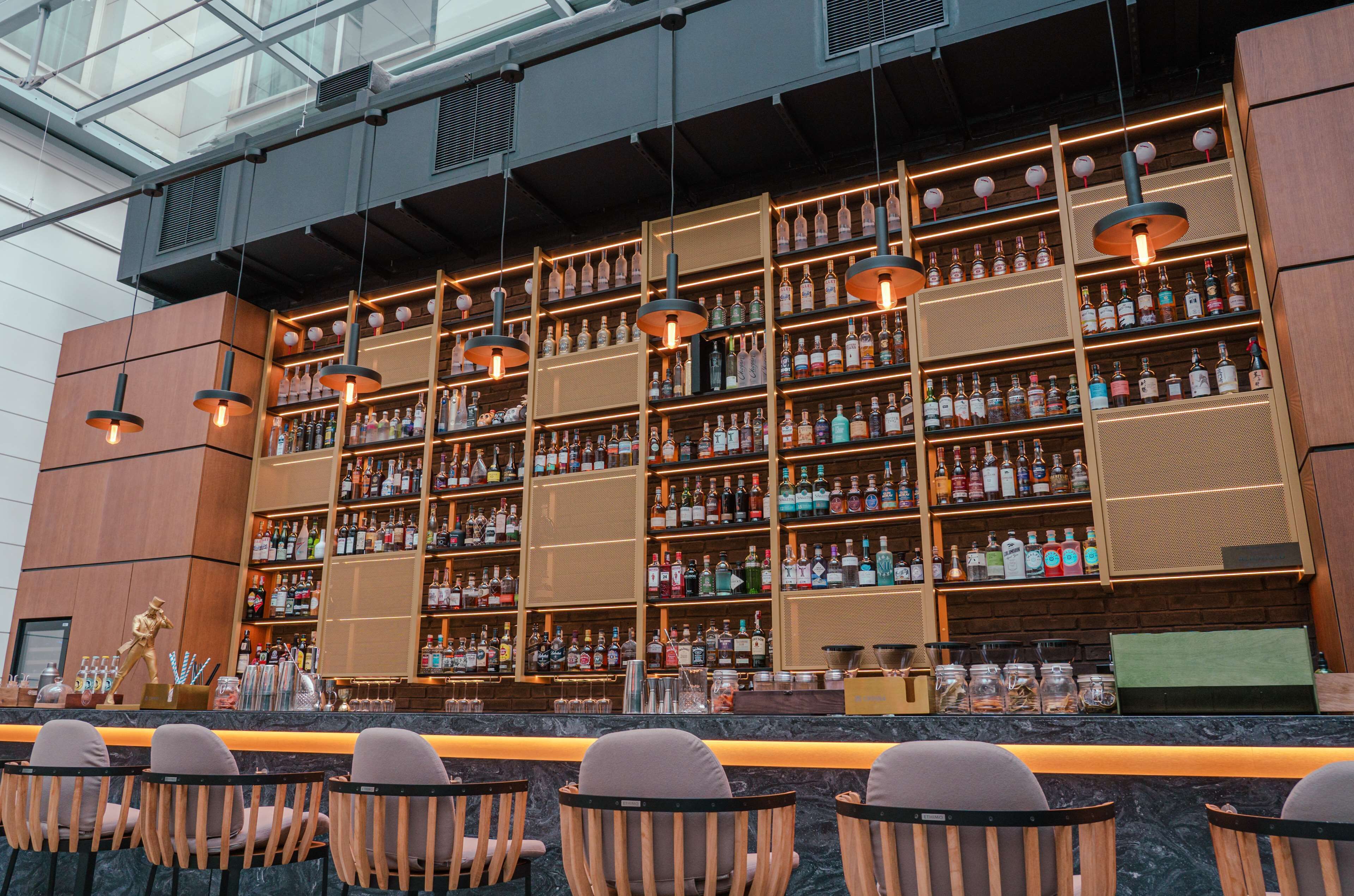 Un bar con varias estanterías llenas de botellas de licor, luces colgantes y taburetes de bar.