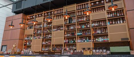 Un bar con varias estanterías llenas de botellas de licor, luces colgantes y taburetes de bar.