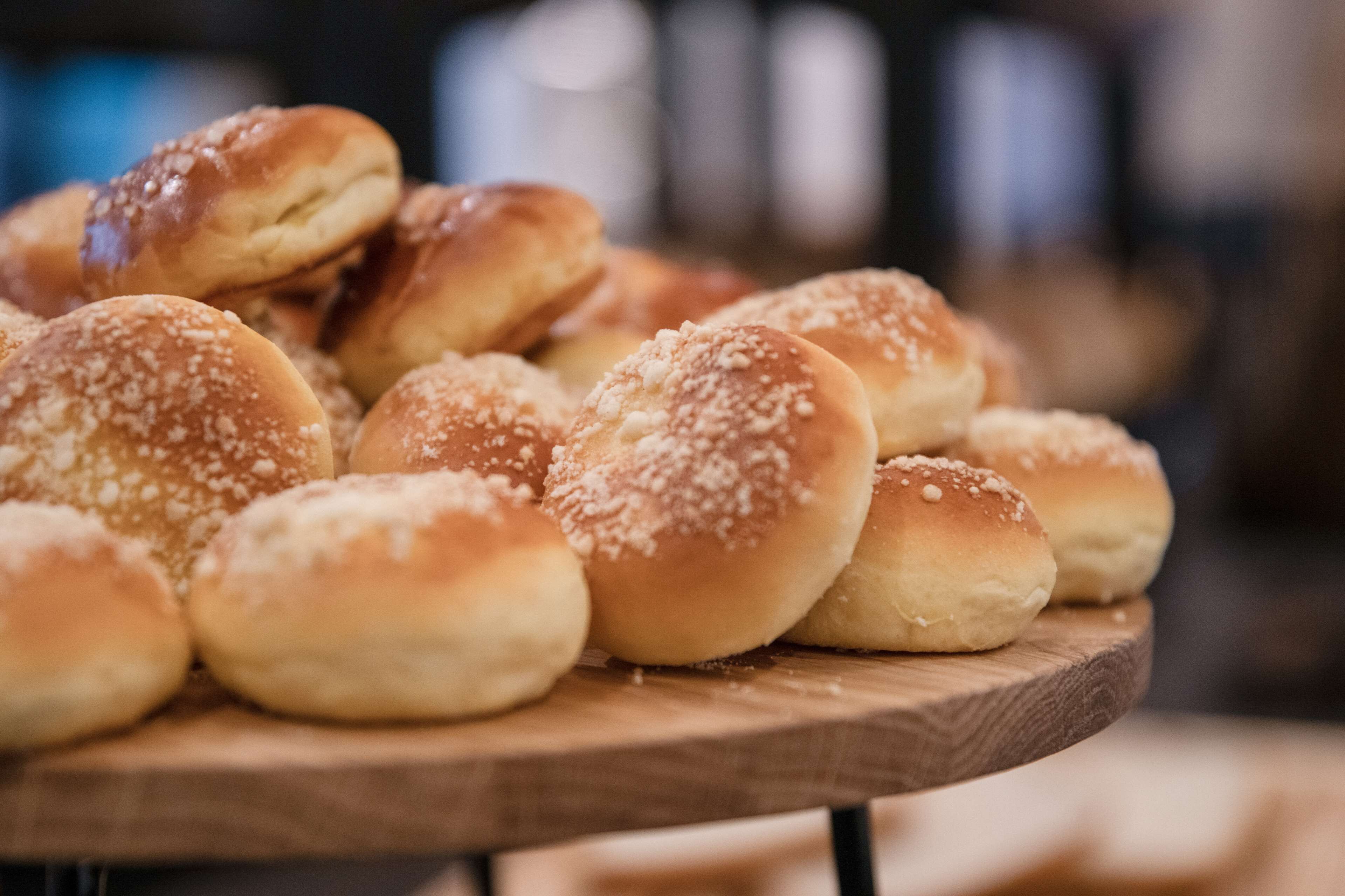 A wooden board with several round, golden-brown buns topped with white granules, likely salt or sugar, on a wooden surface.