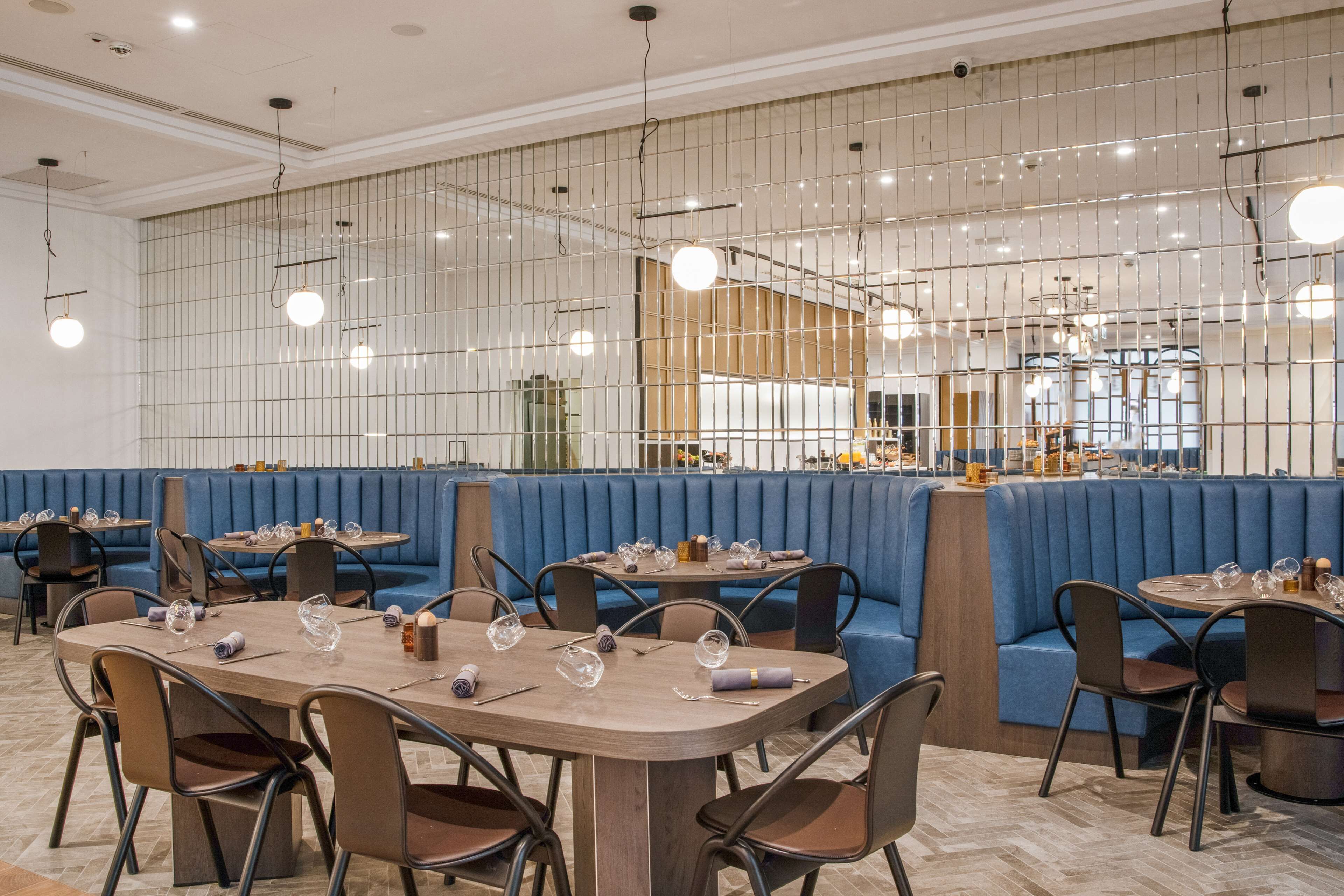 Een modern restaurantinterieur met blauwe zithoeken, houten tafels en hangende吊灯.