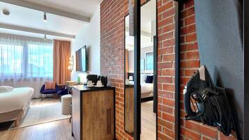 A modern hotel room with a brick accent wall, a large mirror, a bed, a desk with a coffee maker, and a charging station.