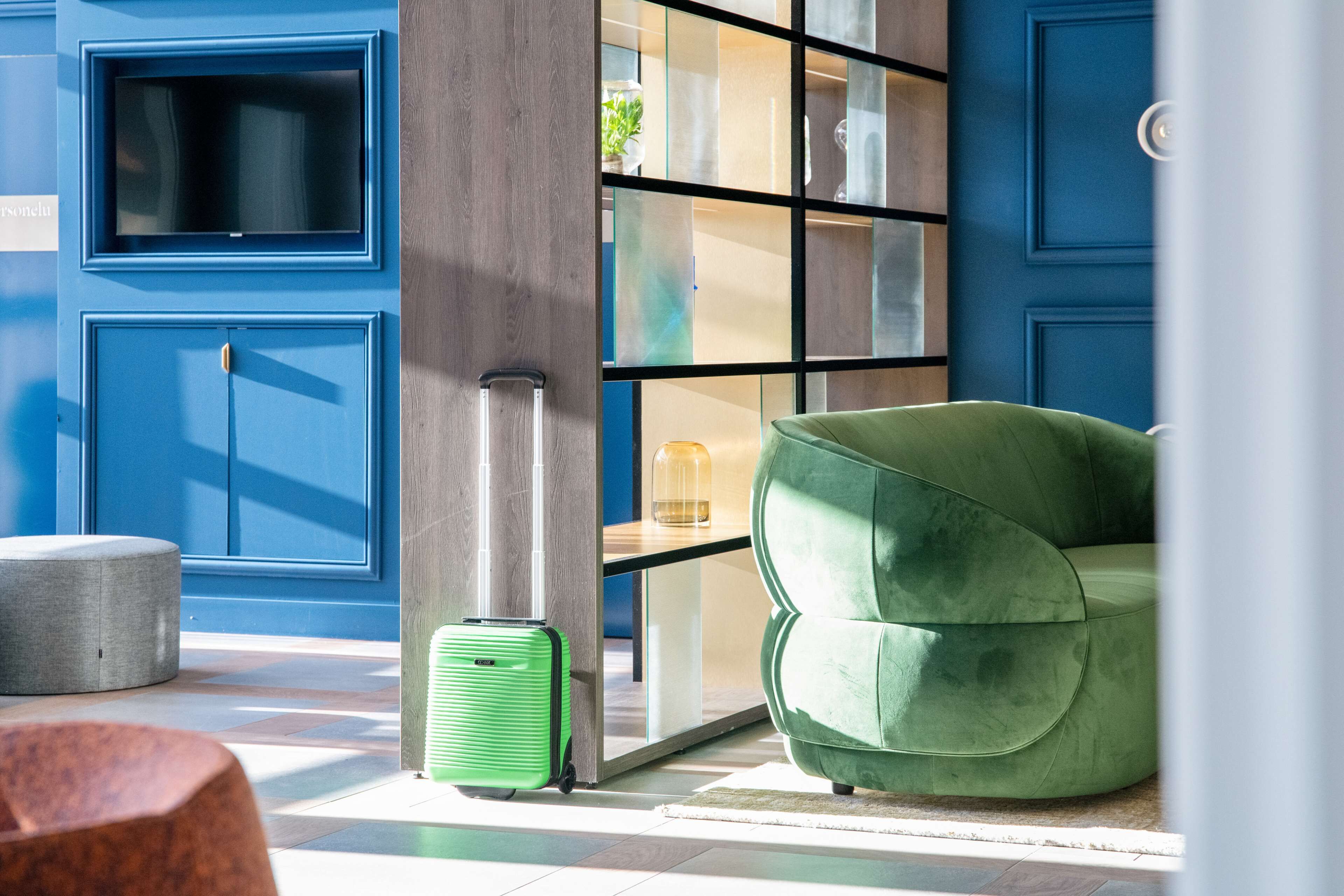 Um hall moderno com um sofá verde, uma mala verde e um banco de madeira.