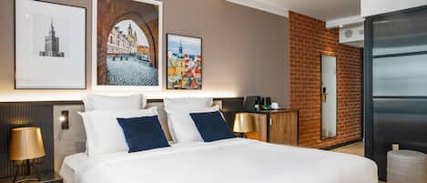 A modern hotel room with a large bed, a nightstand with a lamp, a wooden headboard, and three framed pictures on the wall.