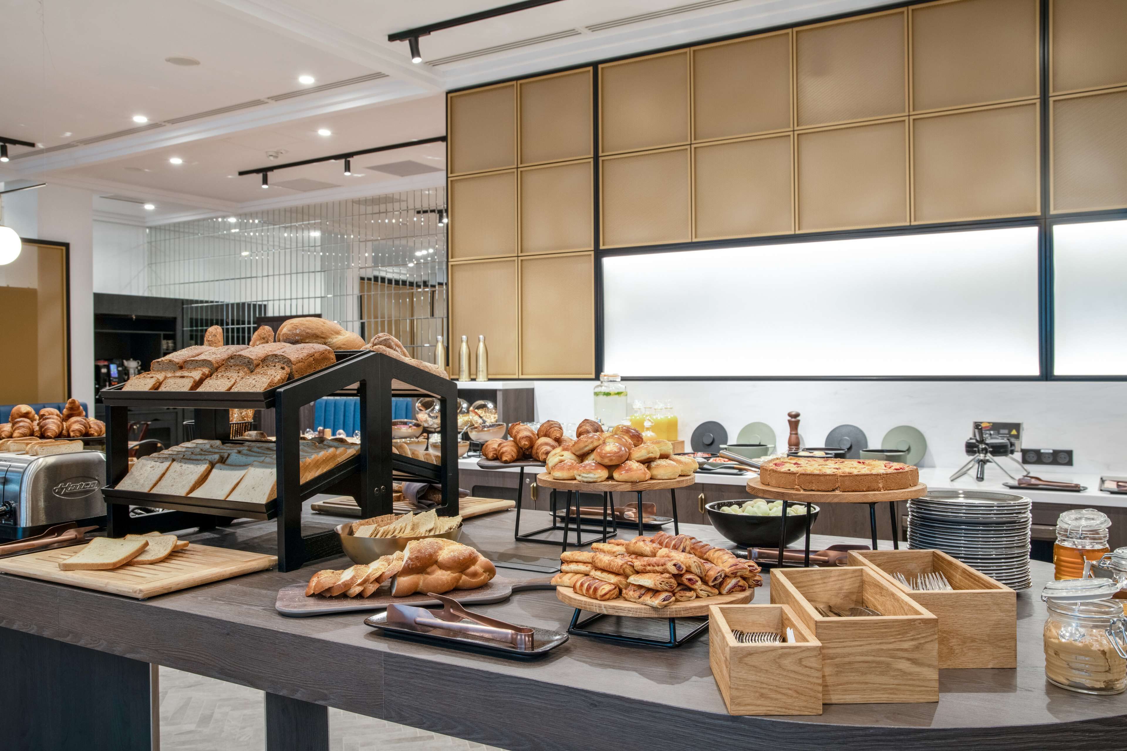 A buffet setup with various breads, pastries, and a fruit bowl.