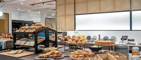 A buffet setup with various breads, pastries, and a fruit bowl.