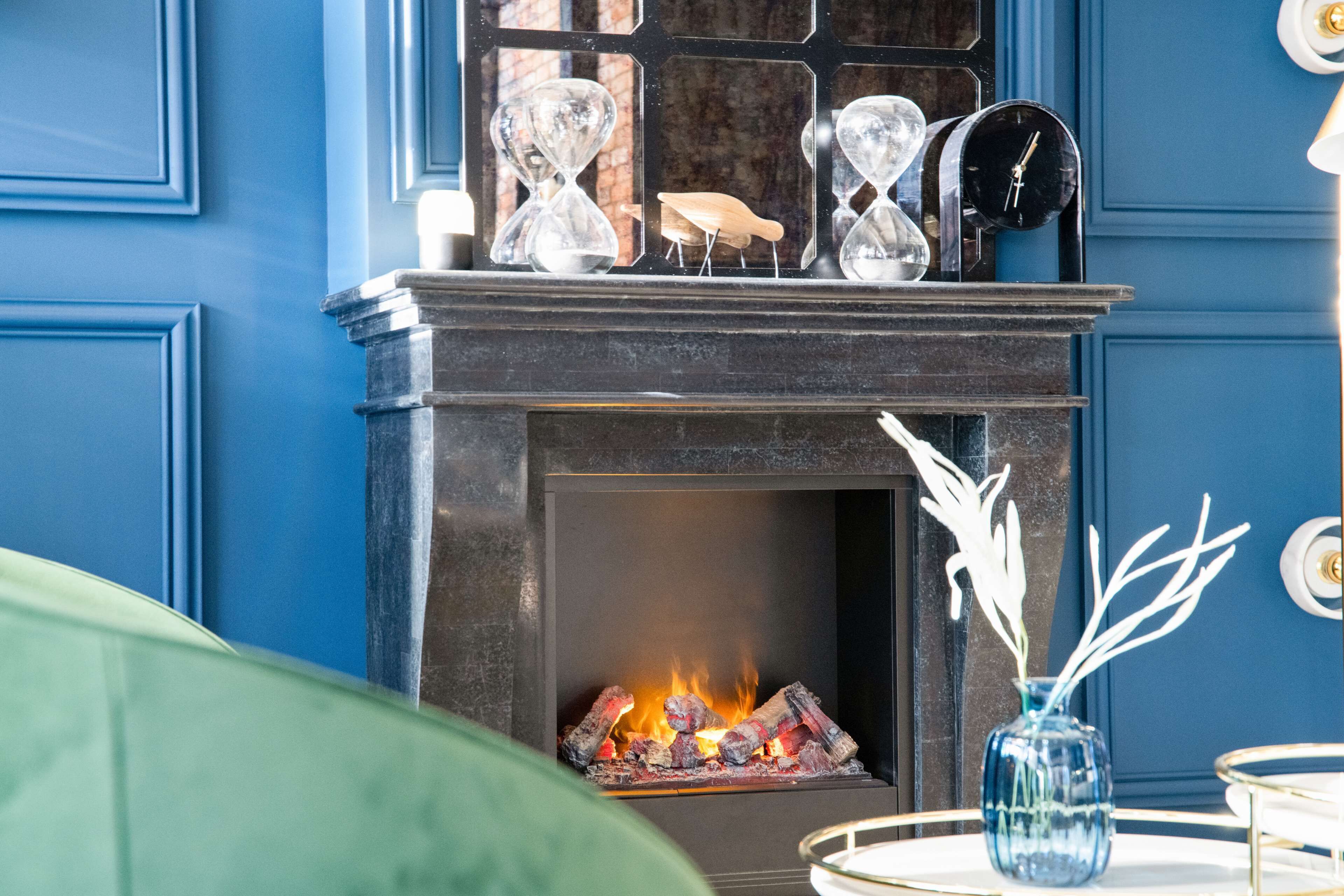 A fireplace with a fire, a clock, and decorative hourglasses on the mantel.