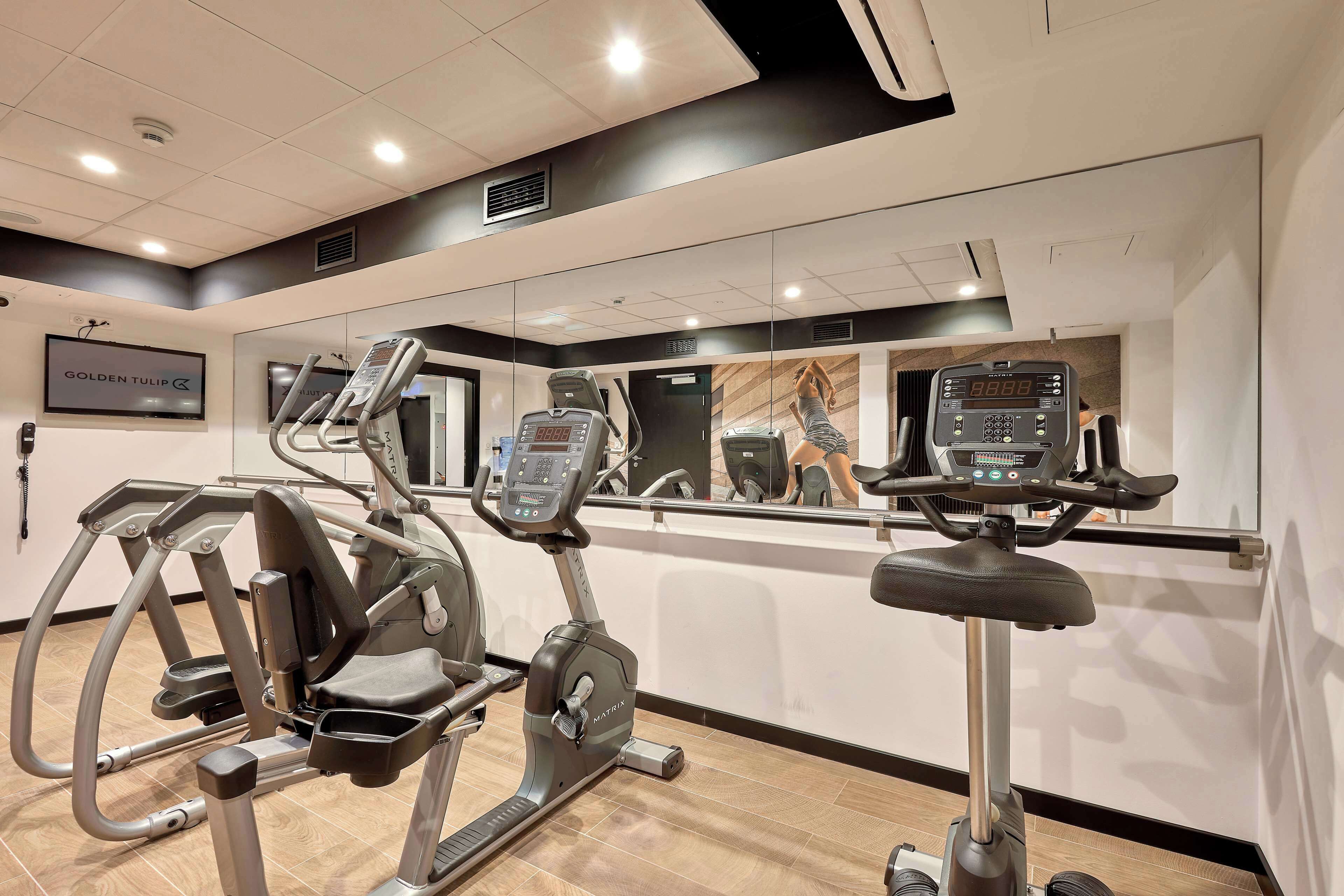 Un gimnasio con equipo de cardio, un espejo grande y un letrero que dice 'GOLDEN TULIP'.