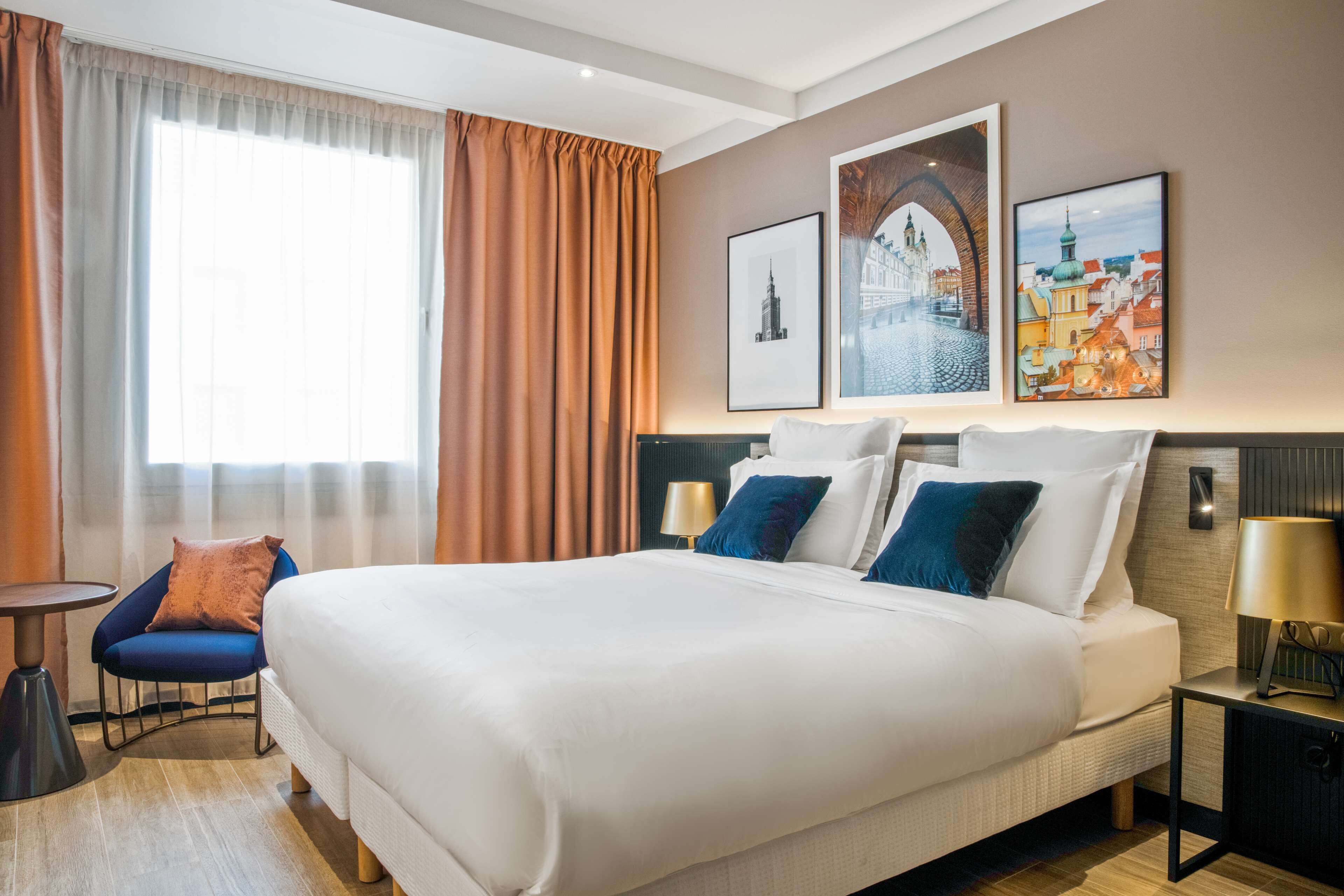 A hotel room with a large bed, a chair, a small table, and two wall-mounted lamps.