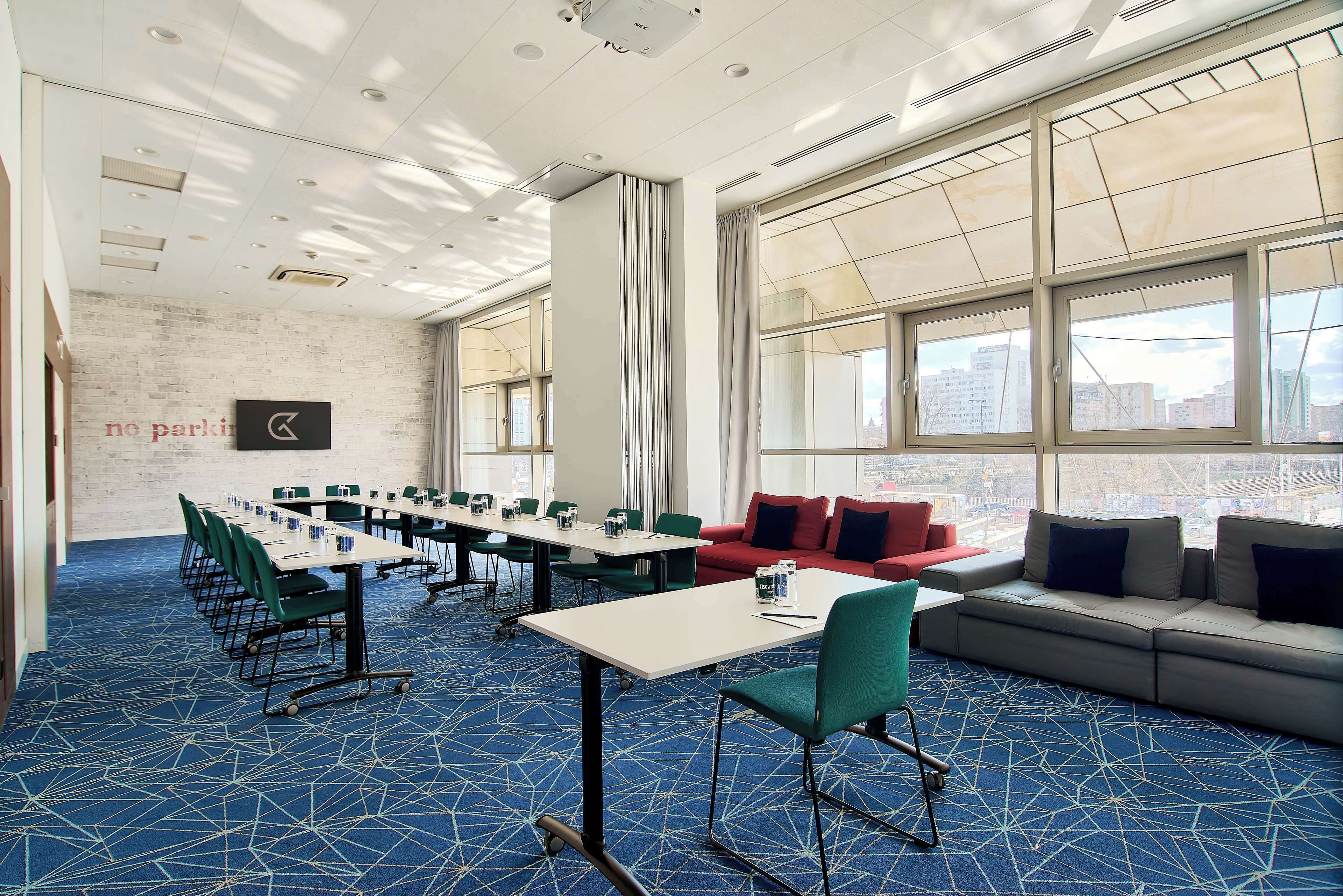 A conference room with a long table, chairs, a sofa, and large windows with a city view.