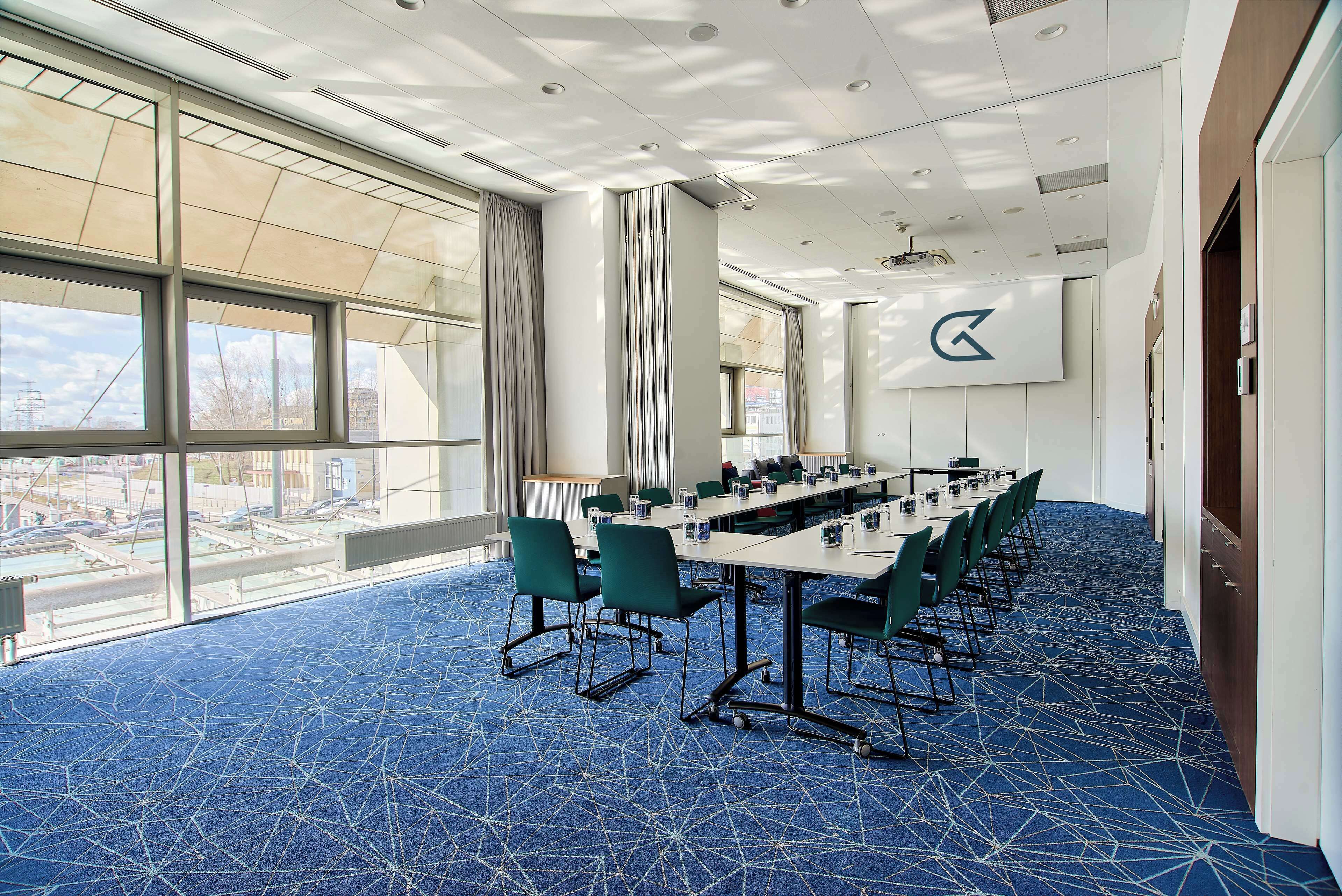 A conference room with a long table, green chairs, and large windows with a city view.