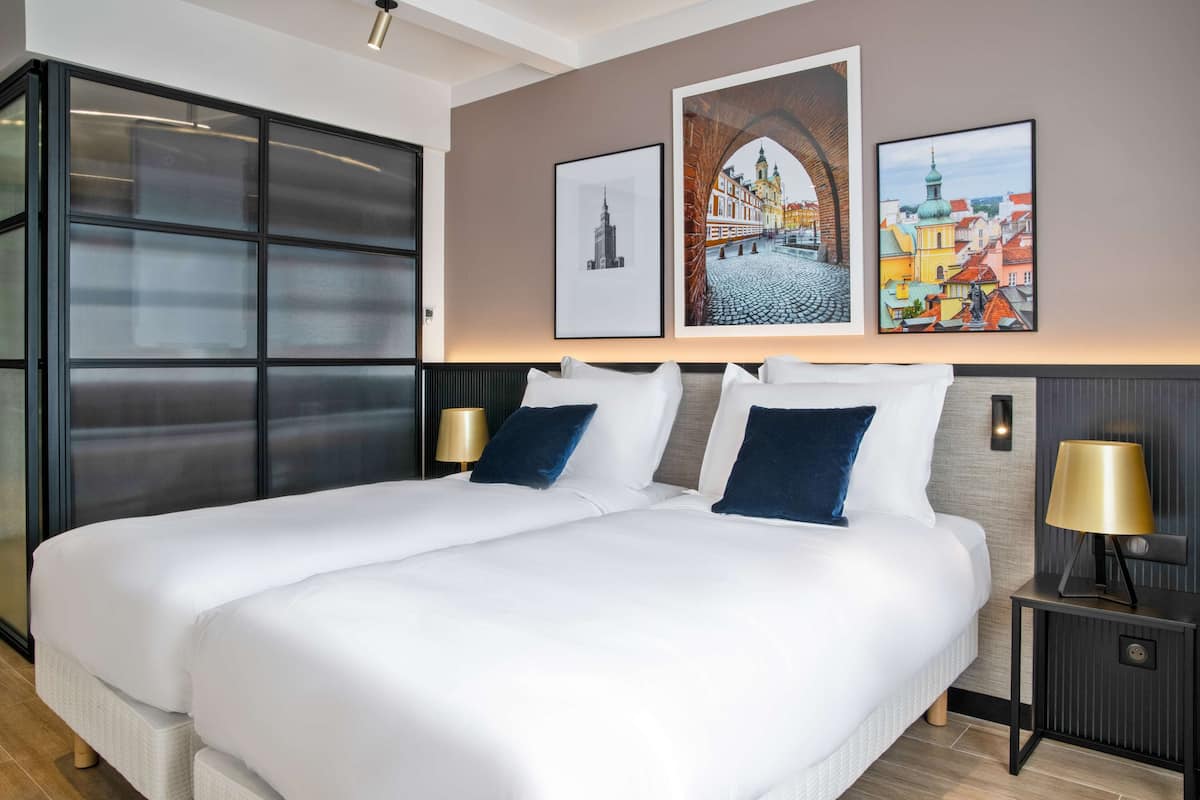 Ein Hotelzimmer mit einem großen Bett, zwei Nachttischen inklusive Lampen und drei gerahmten Bildern an der Wand.