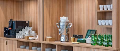 Un coin café équipé d’une machine à café, de tasses et d’une grande cafetière.