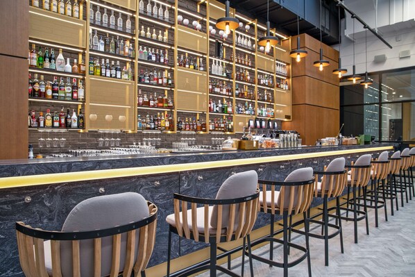A bar area with multiple shelves of liquor bottles, a marble countertop, and several bar stools.