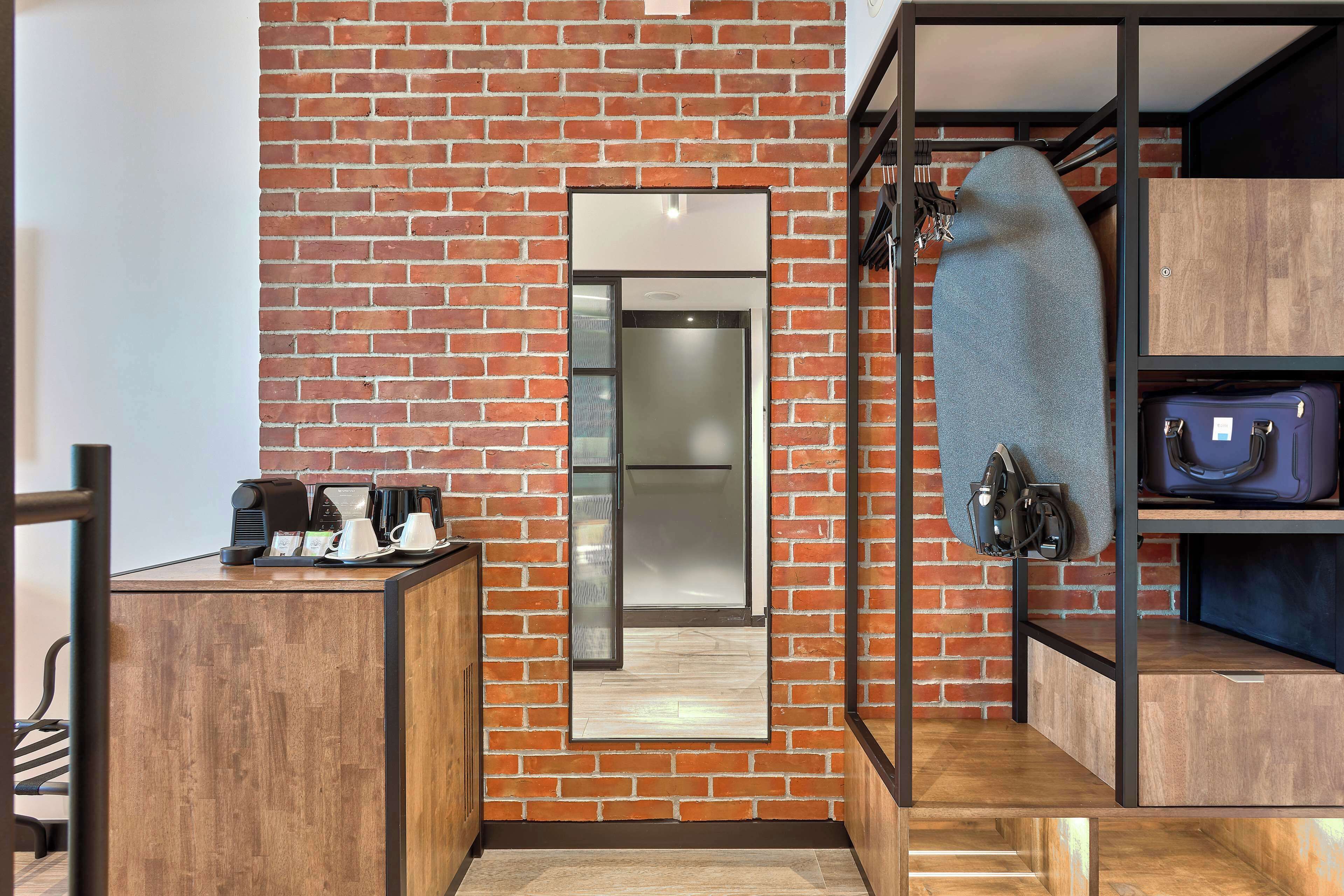 Una habitación compacta con pared de ladrillo, un escritorio pequeño con cafetera y un espejo.
