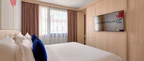 A hotel room with a bed, a TV mounted on the wall, and a window with curtains.