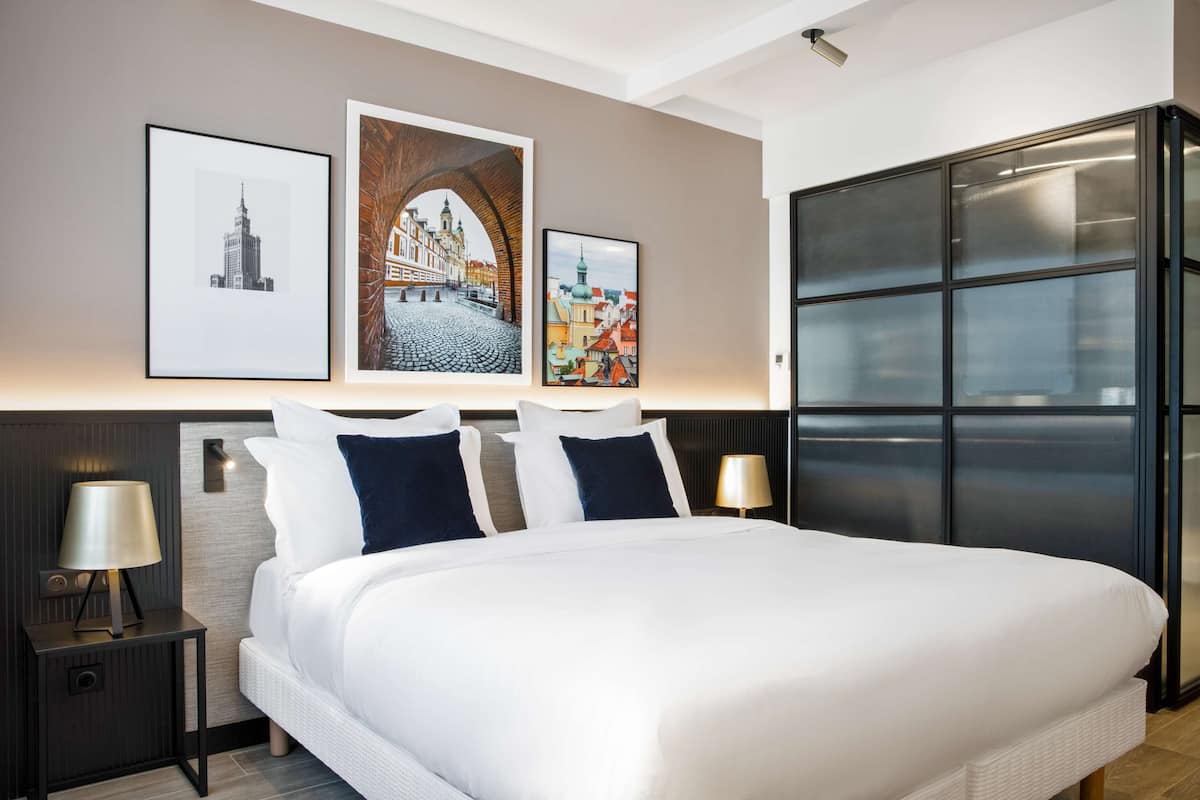 Ein modernes Hotelzimmer mit einem großen Bett, zwei Nachttischen mit Lampen und drei gerahmten Kunstwerken an der Wand.