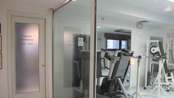 A gym with exercise equipment, a sauna, and a glass door with a sign.