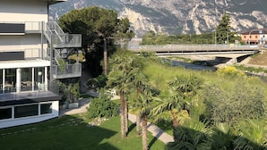 Un edificio moderno con terraza en la azotea, un puente y montañas al fondo.