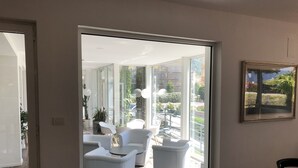 Un interior moderno con un cerramiento de vidrio corredera que da a un balcón con mobiliario exterior y vistas a la ciudad.