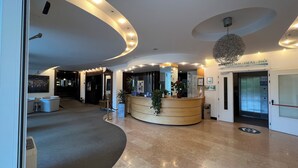 Vestíbulo de hotel con una recepción de diseño curvo, un espejo grande y un letrero que indica las instalaciones de bienestar, sauna y piscina.